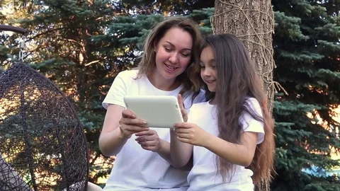 Happy mother and daughter using white tablet PC, sitting in a park at summer day Stock Footage 77291925
