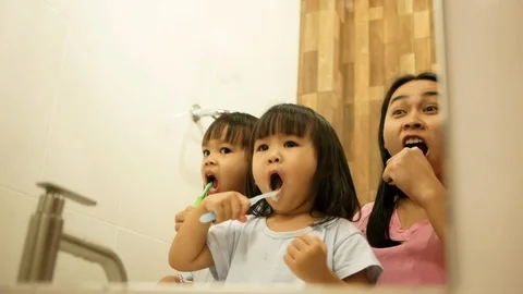 Happy mother and daughters brushing teeth together in the bathroom. Stock Footage