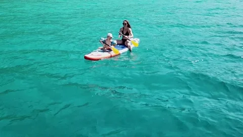 A happy mother and her son sitting on a SUP board. Shot with a drone. 4K Stock Footage 246922053