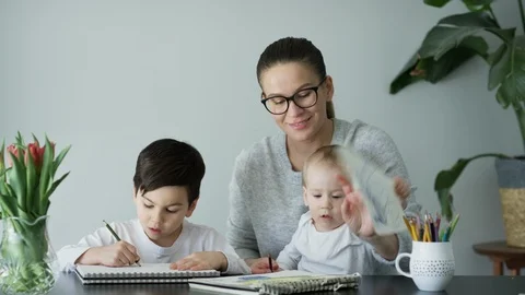 Happy mother holding baby and her son drawing in book at home Stock Footage