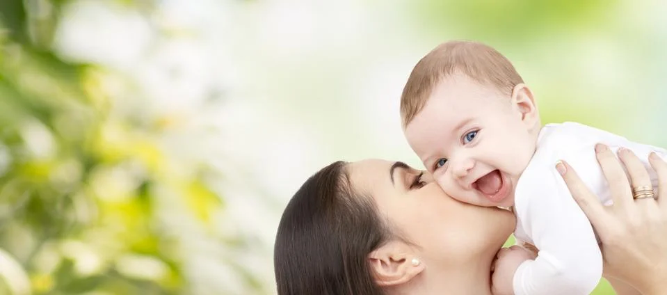 Happy mother kissing baby over green background Stock Photos