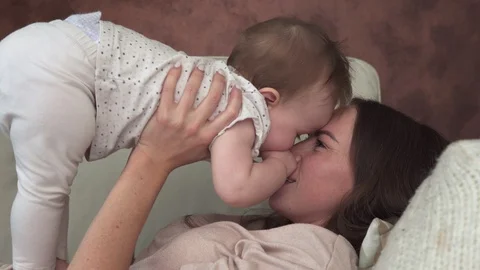 Happy mother lying on sofa smiling and kissing little adorable baby Stock Footage 92140463