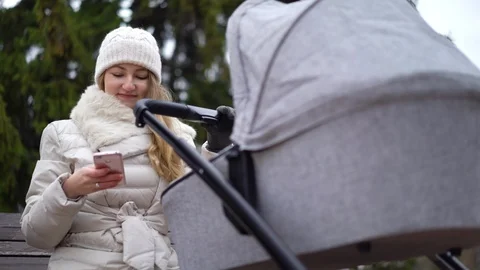 Happy mother with smartphone using app. She sitting on the bench , baby sleeping Stock Footage 120045544