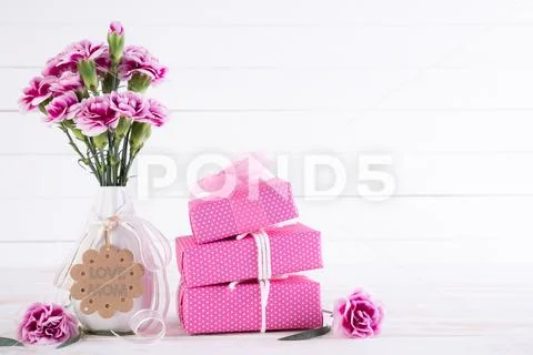 Happy mothers day concept. Gift box with pink carnation flower on white woode Stock Photos