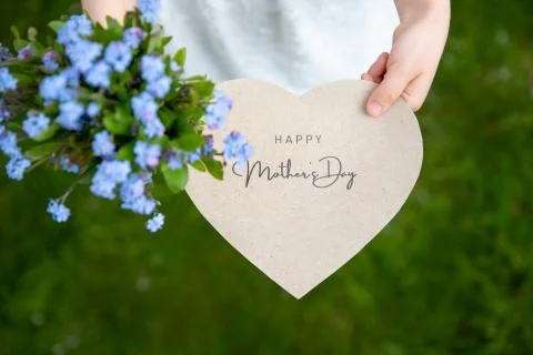 Happy Mother's Day written on a heart-shaped card and nots held by a girl Stock Photos