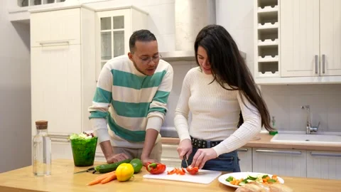 Happy multi ethnic couple cooking healthy food together in the kitchen Stock Footage 334134143