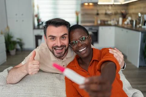 Happy multi-ethnic couple sharing the news of their pregnancy with friends and Stock Photos