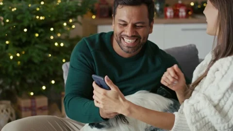 Happy multi ethnicity couple taking picture with dog at home during the Christma Stock Footage 218782272