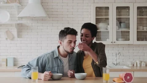 Happy multiethnic couple having breakfast in kitchen. Young couple feed each Video stock 236486000