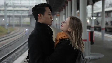 The happy multiethnic couple stands in the train station, talks and hugs Stock Footage 83160432