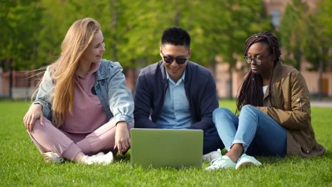 Happy multiethnic students sitting on campus lawn watching video on laptop Stock Footage 141219092