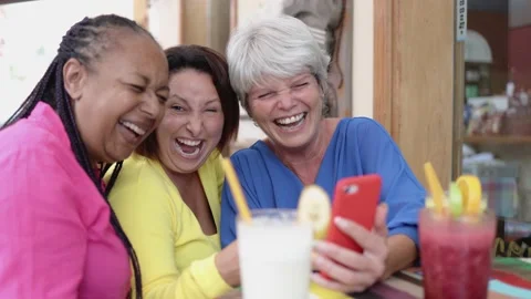 Happy multiracial senior having fun using mobile phone at brunch restaurant - Stock Footage 163374125
