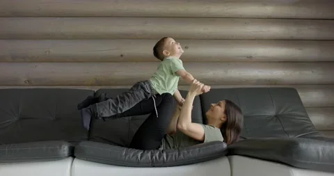 Happy mum lying on her back on a comfortable sofa having fun with a young child Stock Footage 196949006