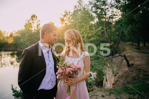 Happy newlyweds standing on the lake shore at sunset Stock Photos