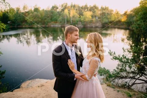 Happy newlyweds standing on the lake shore at sunset Stock Photos