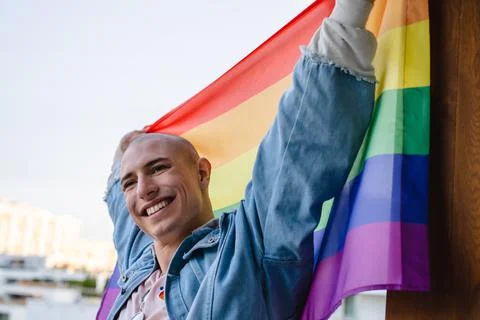 Happy non-binary queer person proudly holding rainbow pride flag and smiling Stock Photos
