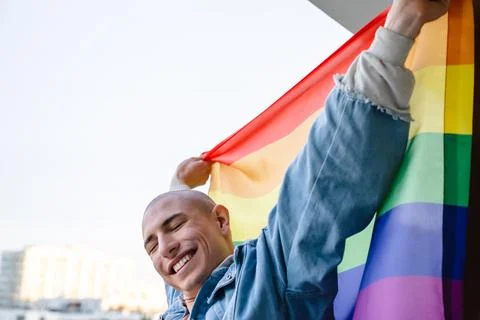 Happy non-binary queer person proudly holding rainbow pride flag and showing Stock Photos