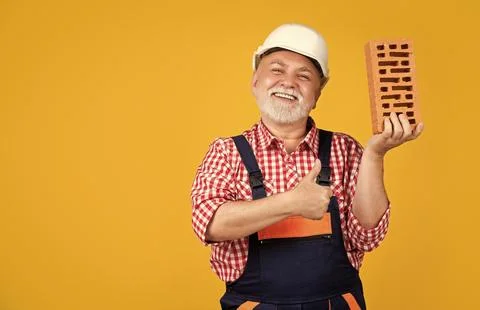 Happy old aged man bricklayer in helmet on yellow background. thumb up Stock Photos