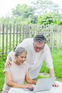 Happy old couple use computer to surf the Internet outdoors Stock Photos