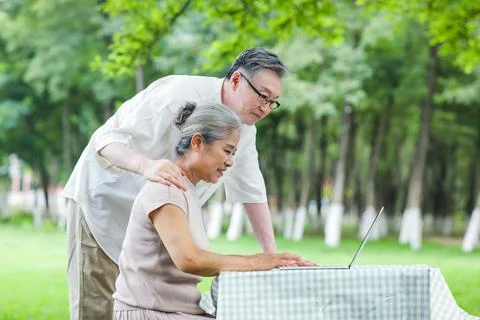 Happy old couple use computer to surf the Internet outdoors Stock Photos
