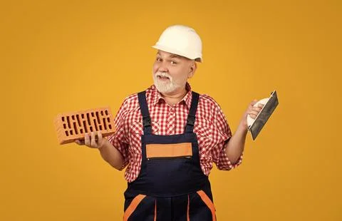 Happy old man bricklayer in helmet on yellow background Stock Photos