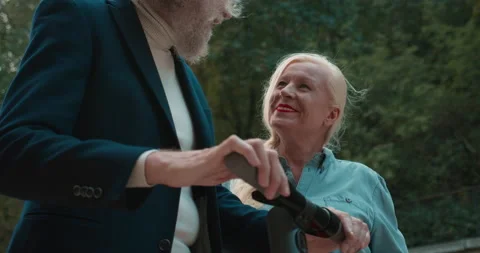 Happy old man explaining how to ride electric scooter to smiling lady on a date Stock Footage 144951626