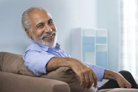 A HAPPY OLD MAN LOOKING AT CAMERA WHILE RELAXING AT HOME Stock Photos