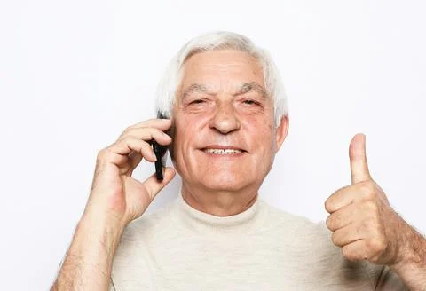 Happy old man using smartphone and show thumbs up desture over white background. Stock Photos