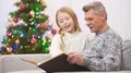 The happy old man watch the photo album with a girl near the christmas tree 4k or 4k+ Resolution