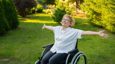 Happy old woman spread her arms to the sides while sitting in a wheelchair on a Stock Fotos