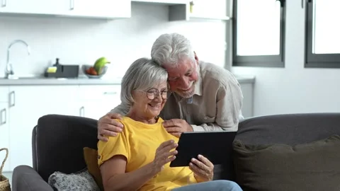 Happy older couple using computer tablet together at home, excited mature man an Stock Footage 237941412