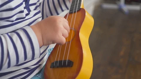Happy one year old boy plays his guitar or ukulele and sings songs, sitting in Stock Footage 97223086