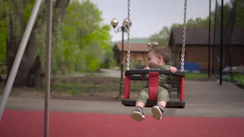 A happy one year old boy swings on a swing and laughs. Little child on the Stock Footage 241459924