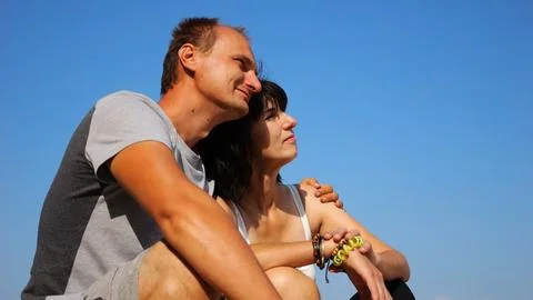 Happy pair hugs during sitting on wooden log on beach. Romantic couple admi.. Stock Photos
