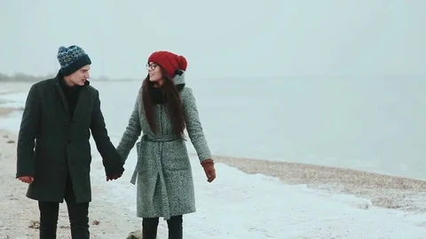 Happy pair, on warm clothes, walk outside on coast sea, behind gray sky Stock Footage 70994225