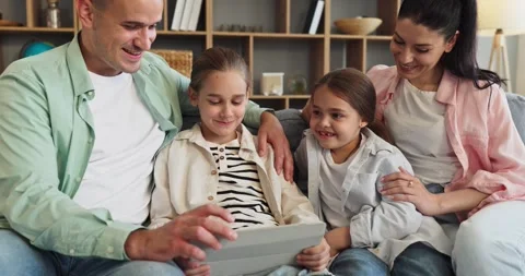 Happy parents and daughters using digital tablet together on couch at home Stock Footage 343406377