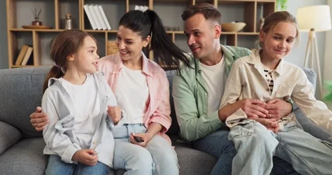 Happy parents and two daughters bonding on sofa at cozy home interior together Stock Footage 344833041
