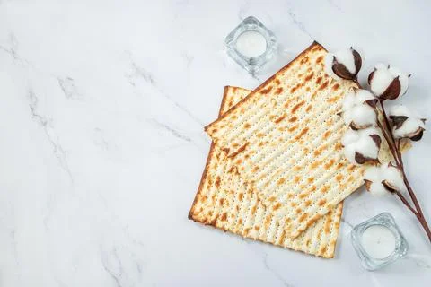Happy Passover concept. Matzo bread and cotton flowers on a white marble. Bac Stock Photos