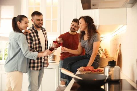 Happy people drinking wine while cooking food in kitchen Stock Photos