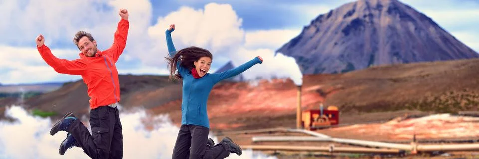 Happy people on Iceland travel adventure jumping of joy at geothermal plant Stock Photos