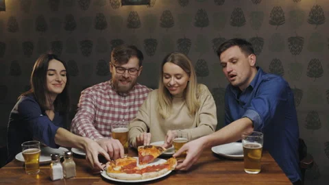 Happy people in pub sit at the table and take their pieces of pizza talking with Stock Footage 147742018