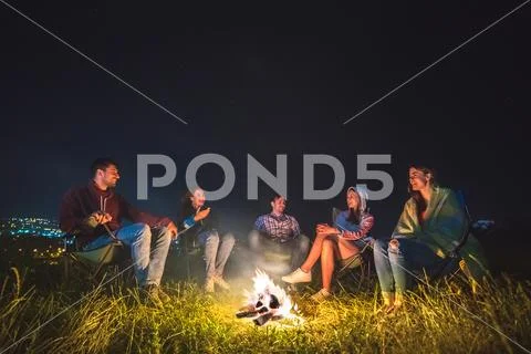 The happy people sit near the bonfire on the background of the city. night ti Stock Photos