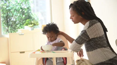 Happy playful Black mother and daughter at feeding time in high chair Stock Footage