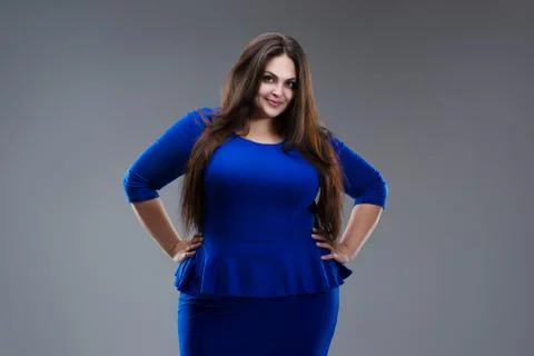 Happy plus size model in blue dress, fat woman with long hair on gray backgro Stock Photos