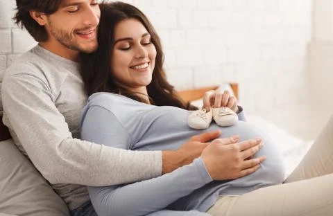 Happy pregnant couple playing with tiny shoes for their future baby Stock Photos