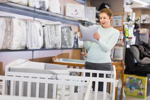 Happy pregnant female customer is buying pillow for crib Stock Photos