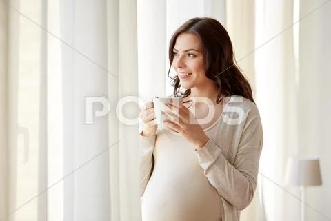 Happy pregnant woman with cup drinking tea at home Stock Photos