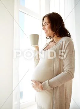 Happy pregnant woman with cup drinking tea at home Stock Photos