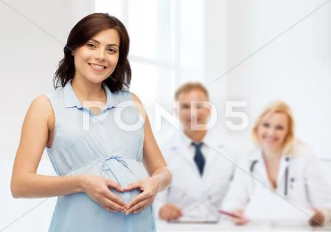 Happy pregnant woman making heart gesture on belly Stock Photos
