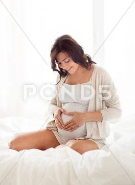 Happy pregnant woman making heart gesture at home Stock Photos